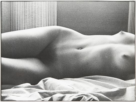 Photo of a nude woman lying on a sheet, visible from breasts to thighs