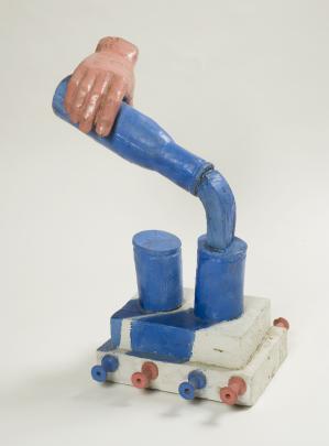 Wooden sculpture of hand pouring blue liquid from blue bottle into one of two blue glasses