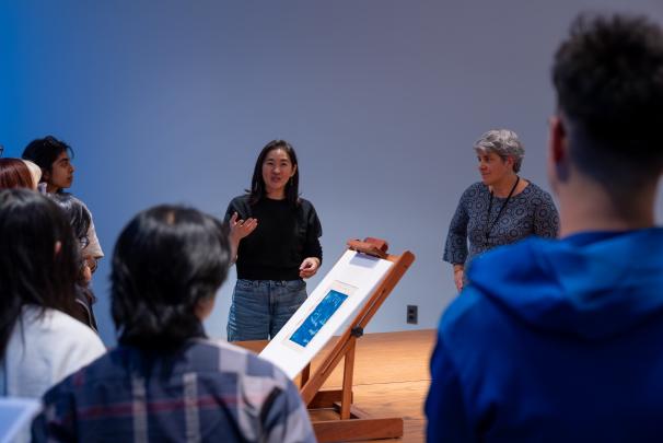 Visitors look on as a artist discusses artwork on display in a research room.