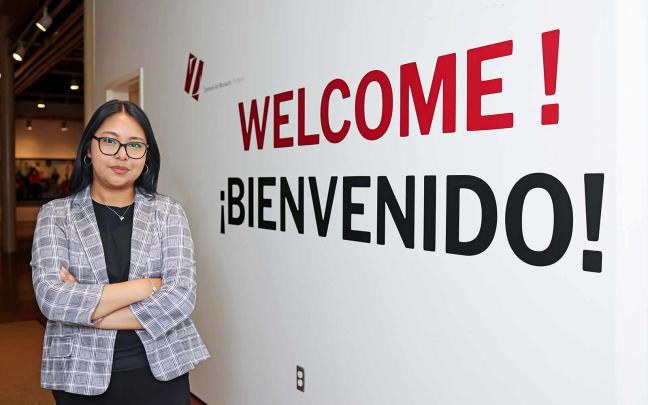 Jessie Garcia, a museum educator, stands next to a bilingual wall greeting inside the Zimmerli.
