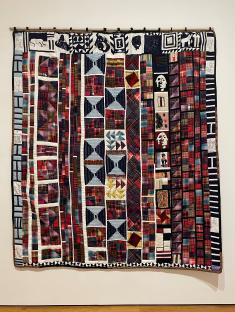Quilt with main panel made of various plaid patches and a border of images of important Black figures and symbols.
