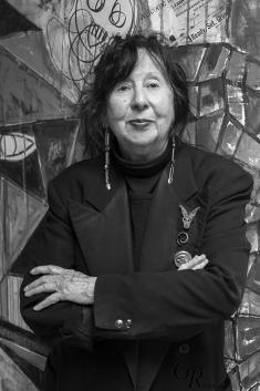 Jaune Quick-to-See Smith, an older Native American woman, stands with her arms crossed dressed in all black.